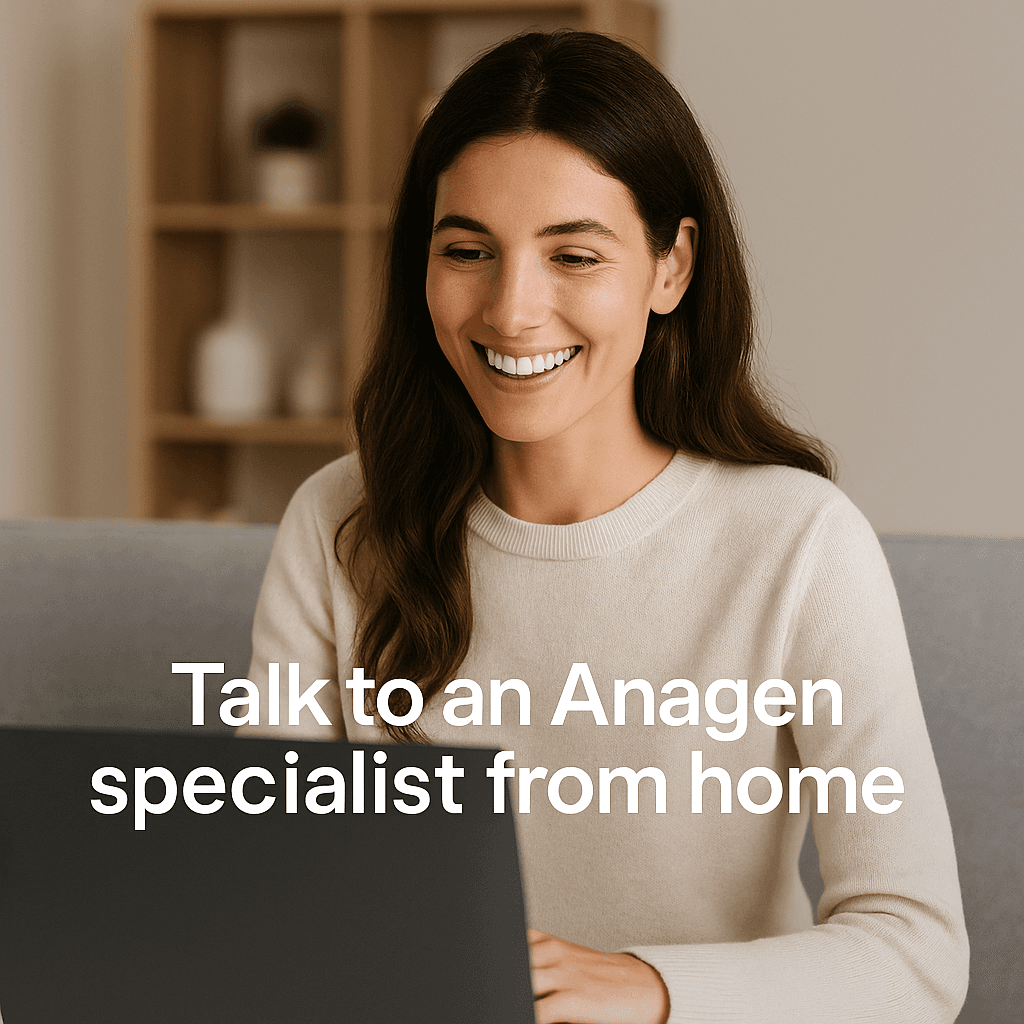 A smiling young woman with long brown hair sits at home, looking at her laptop during a telehealth consultation. She wears a cream sweater in a bright, modern living room. Bold text overlay reads: “Talk to an Anagen specialist from home,” emphasizing the convenience of online hair restoration support.